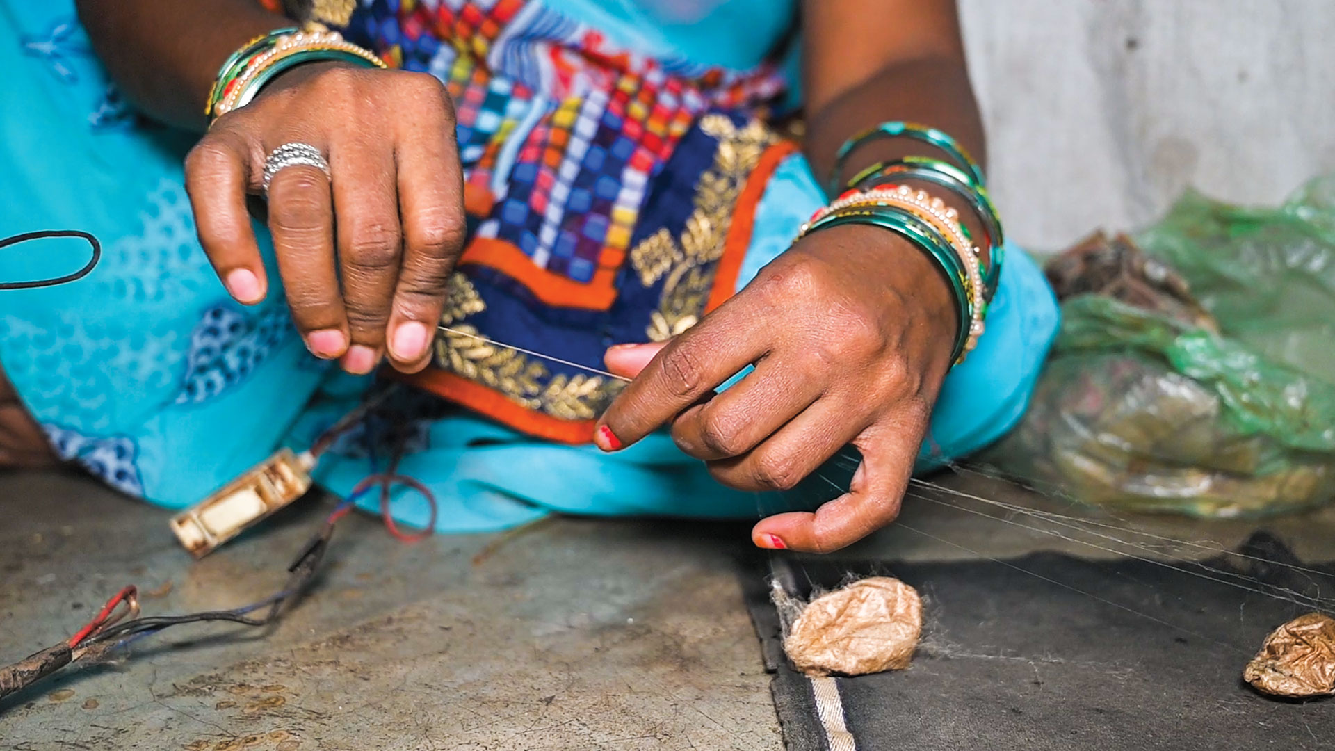 A woman, using her hand, threading directly from a silk worm cocoon